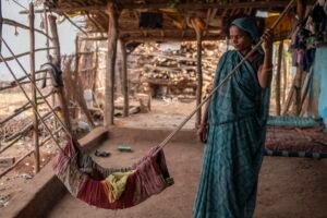 Korku tribal mother in rural Madhya Pradesh gently swinging her infant in a homemade cloth cradle.